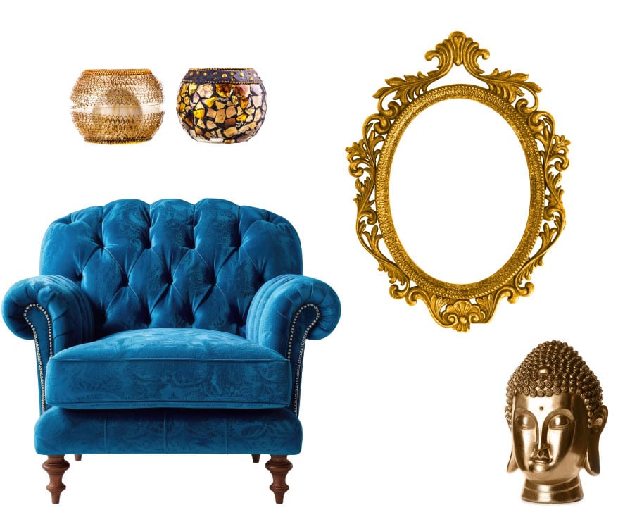 A blue velvet tufted armchair is surrounded by decorative items: two mosaic candle holders, an ornate gold oval frame, and a golden Buddha head statue. The arrangement is against a plain white background.